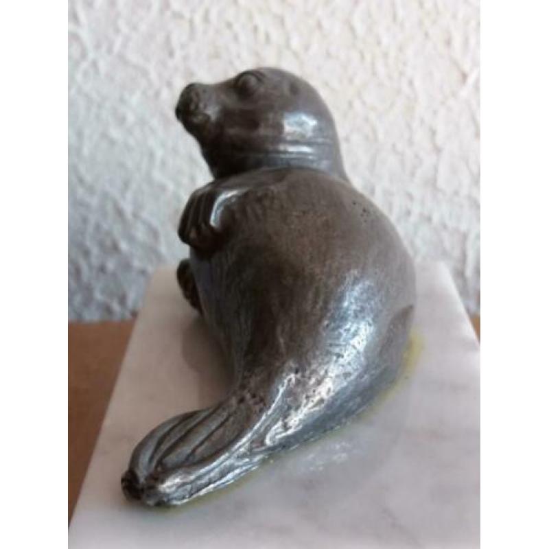 Tinnen zeehondje op een marmeren ondergrond.
