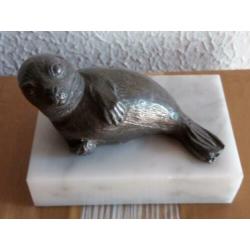 Tinnen zeehondje op een marmeren ondergrond.